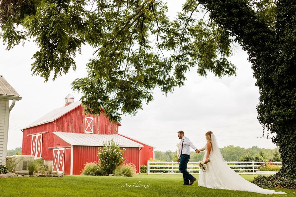 Bride and groom walking hand in hand past the red barn at Barn 1888