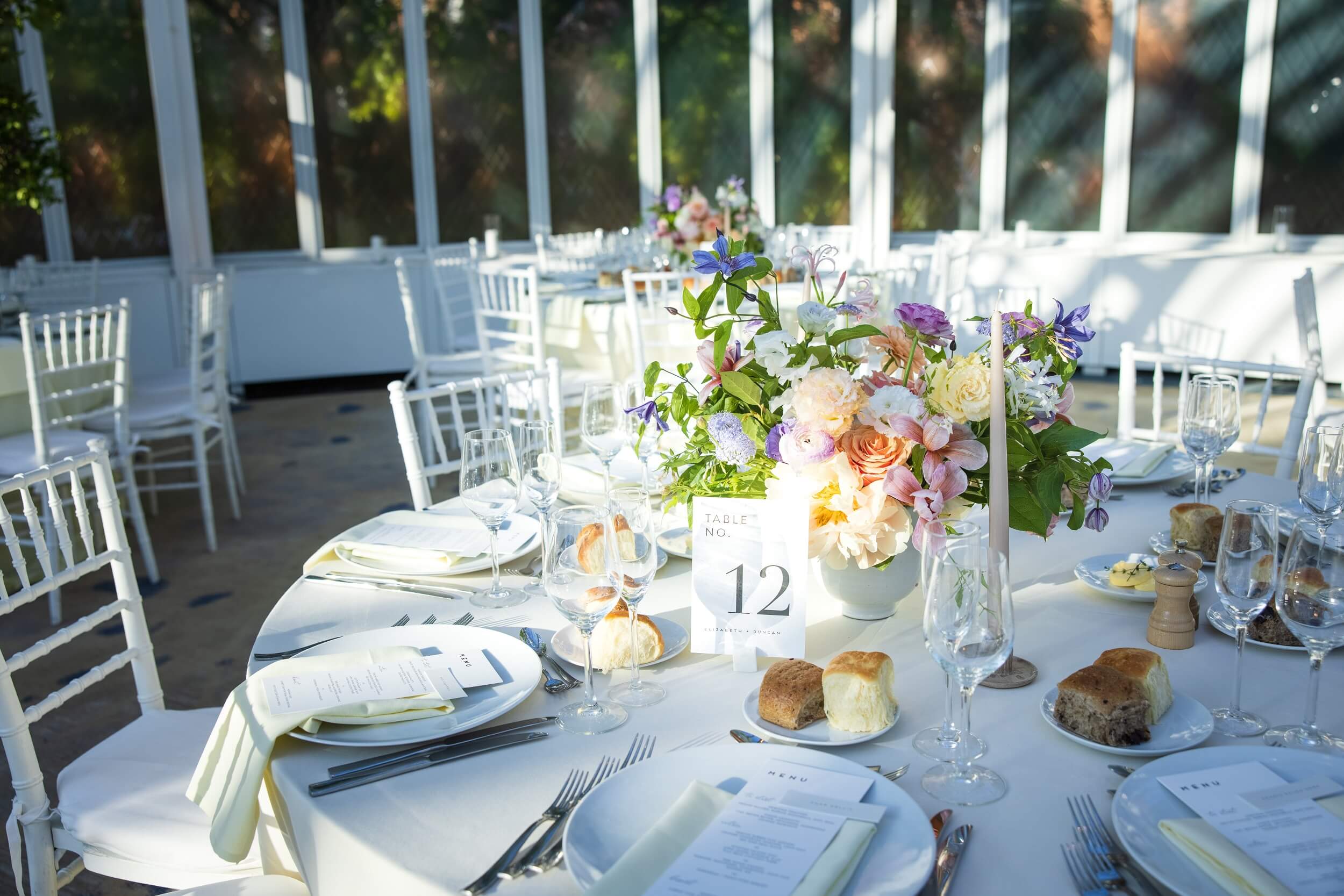 Wedding reception table set with white linen, glassware and a floral centrepiece