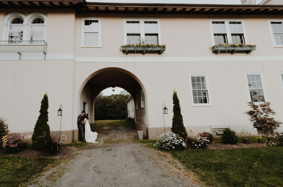 A bride and groom under the archway of a white country house