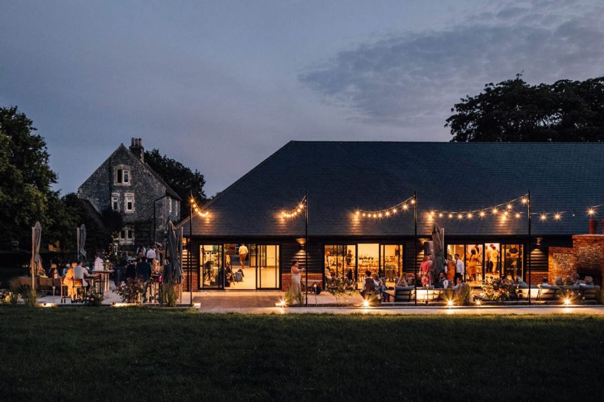 Chapel House Estate's barn venue lit up at twilight with guests outside