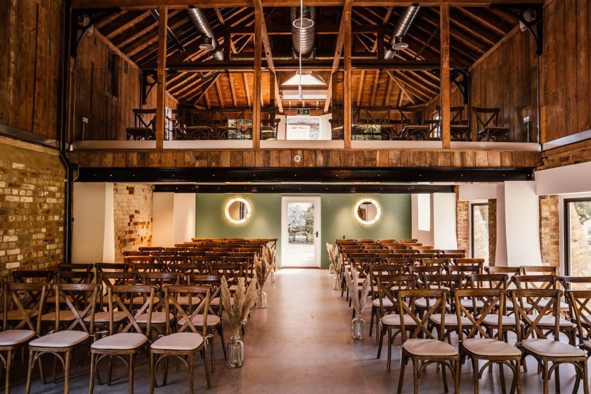 Timber-beamed ceremony barn at Chapel House Estate with rows of cross-back chairs