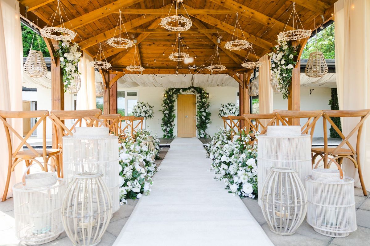 Covered ceremony aisle decorated with white flowers and rattan chandeliers at The Orchard
