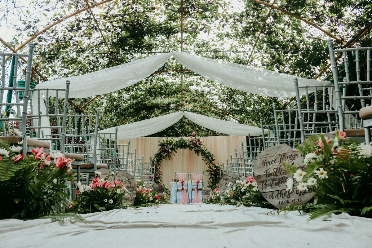 Wedding ceremony under a greenhouse-style marquee with draped fabric and a floral arch