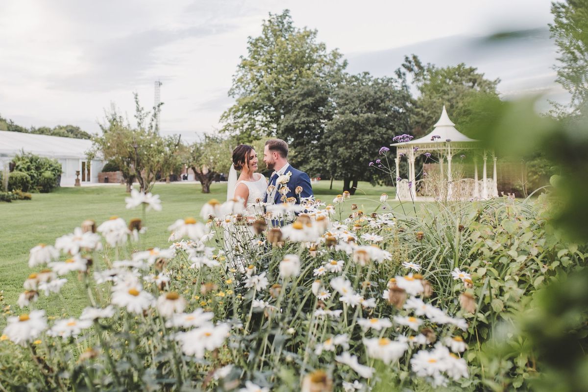 Couple embracing in the gardens at a Tabor Group venue with daisies and a bandstand