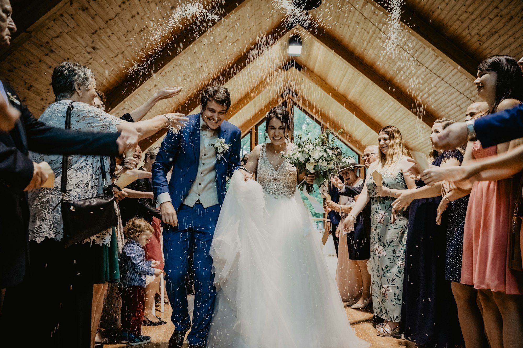 Guests showering a newlywed couple with confetti in a timber-vaulted venue