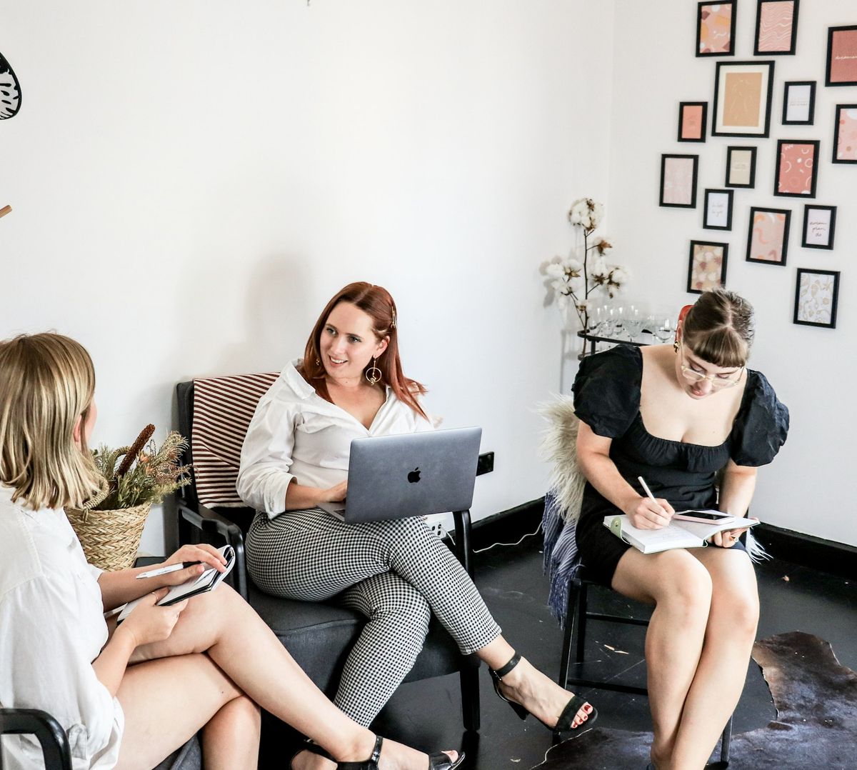 Three colleagues in an informal meeting, one taking notes on a laptop