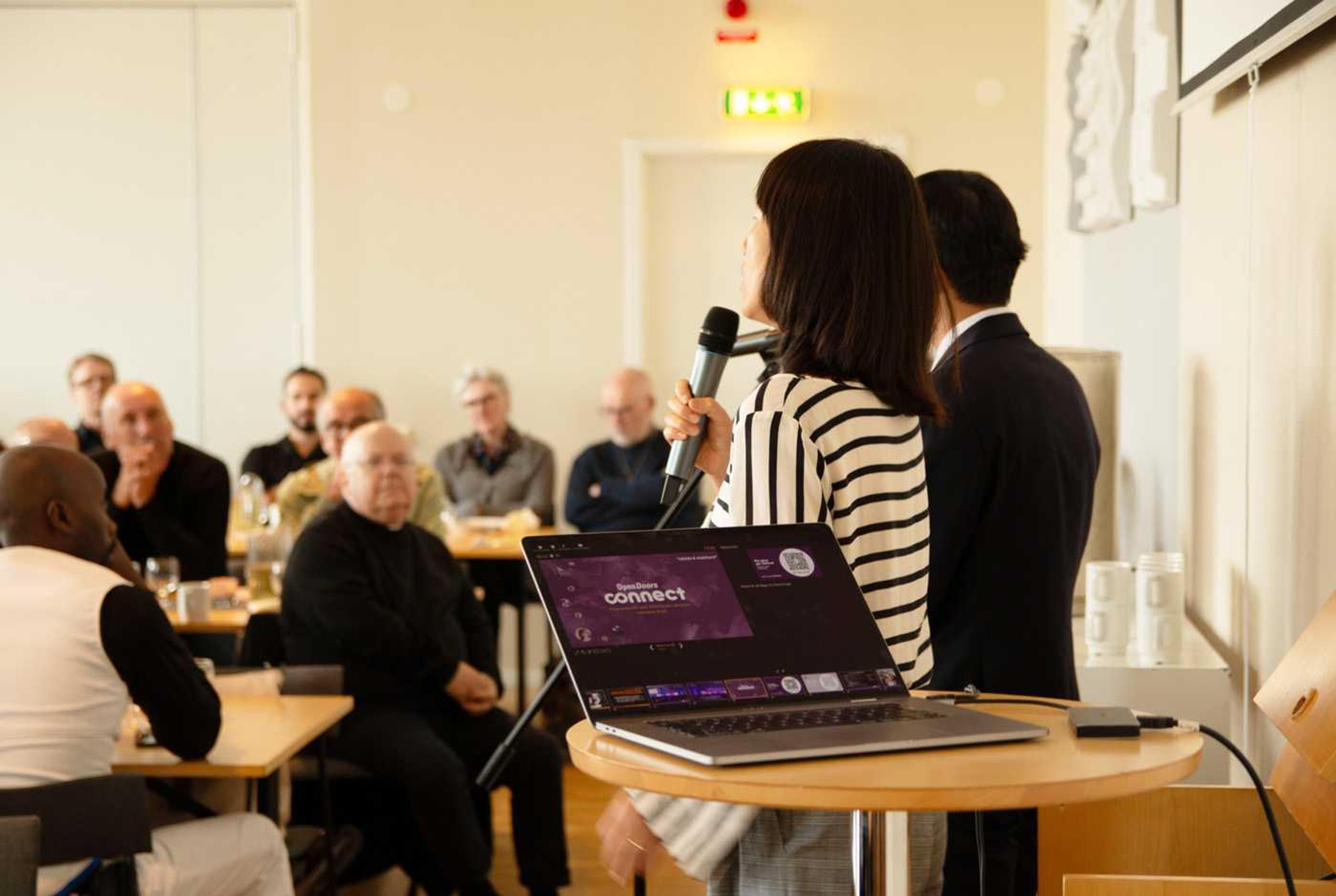 Kyong-So (delvis skymd bakom tolken) talar på en brunch under konferensen Connect i Jönköping hösten 2024.