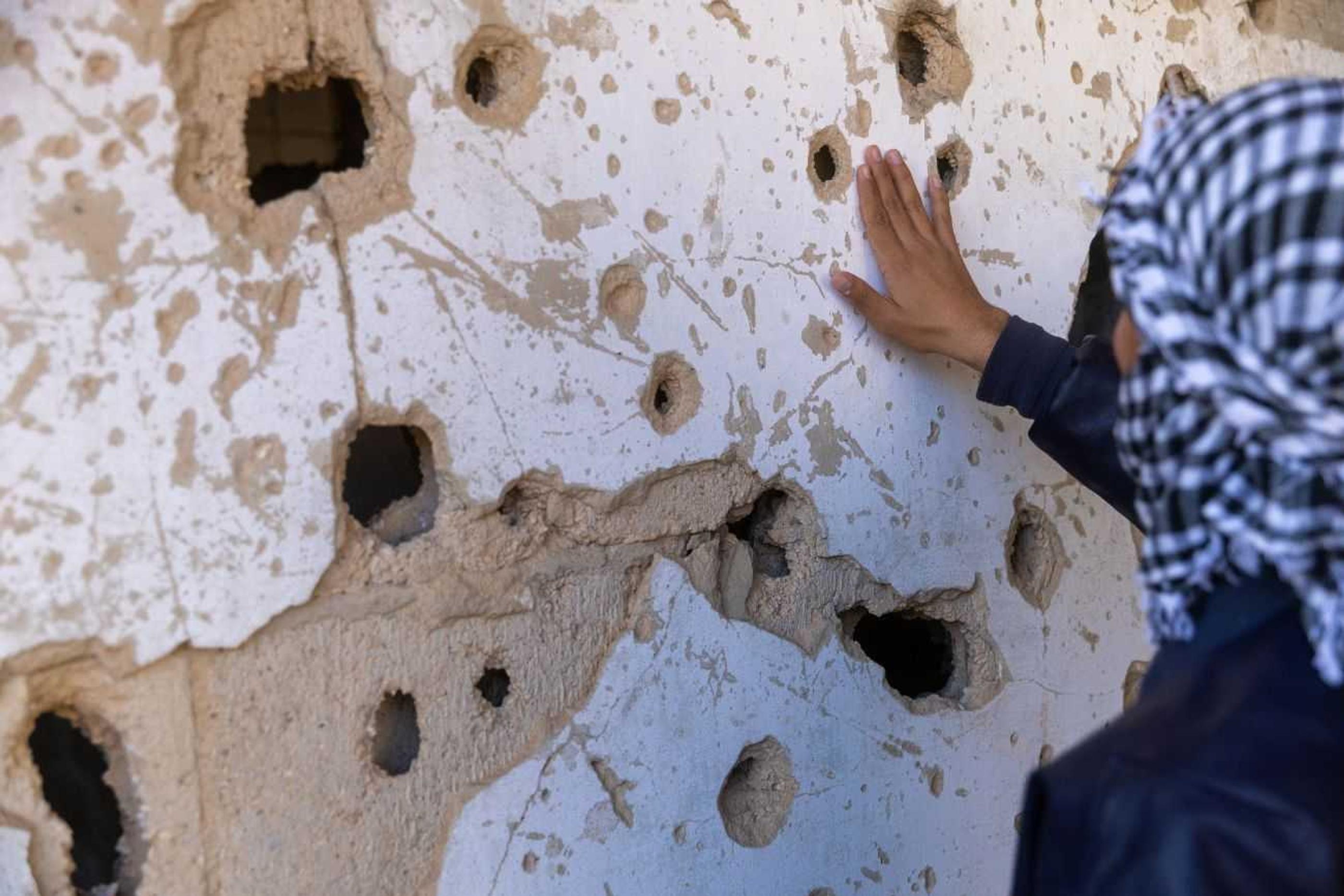 Zaid places his palm on a wall of bullet holes