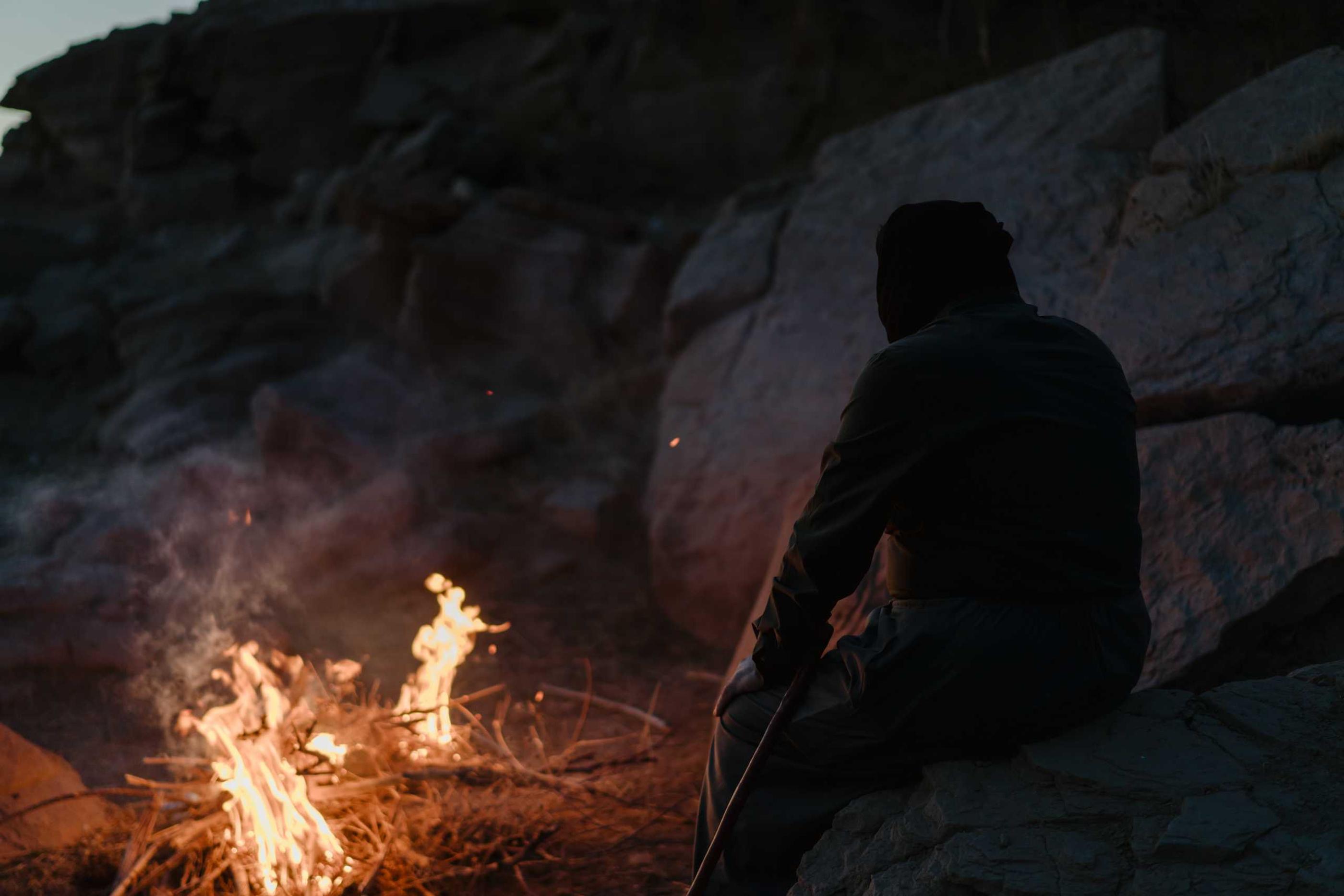 Yasin sitting by a campfire at twilight