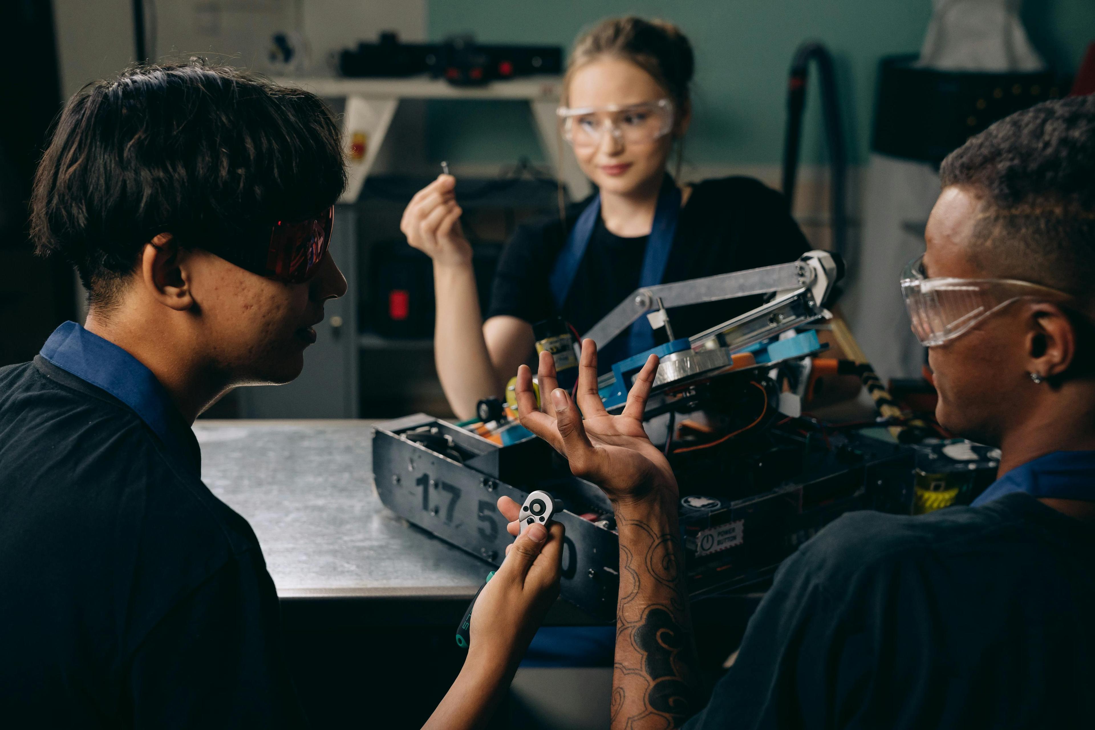 Three engineers collaborate in an indoor workshop on robotics assembly and programming.