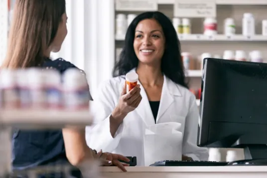 Female pharmacist holding prescription bottle behind pharmacy counter