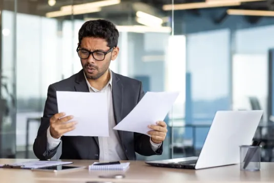 Professionally dressed man looking at papers with confused facial expression
