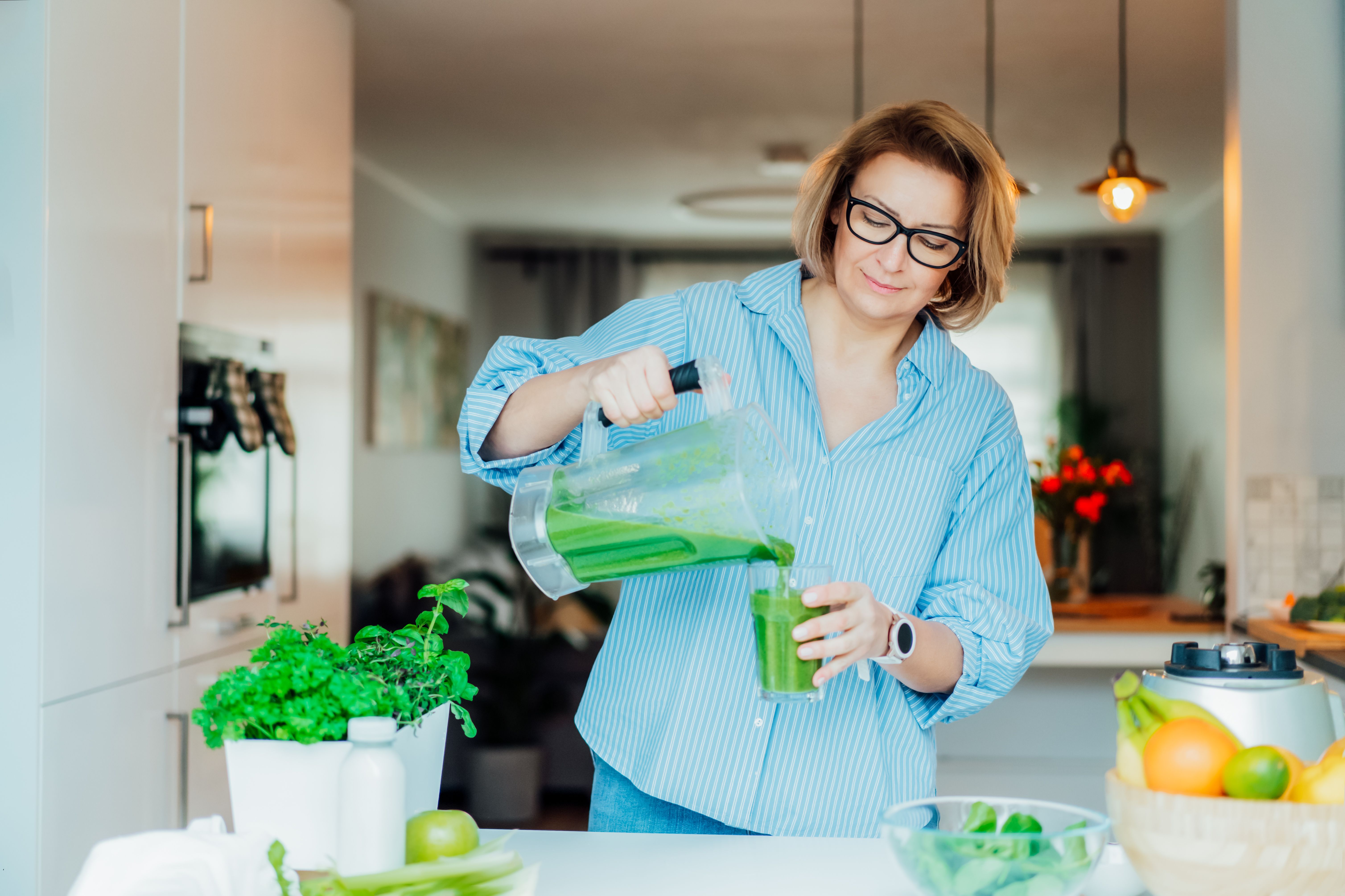 Woman in her kitchen making a green juice smoothie for her health.