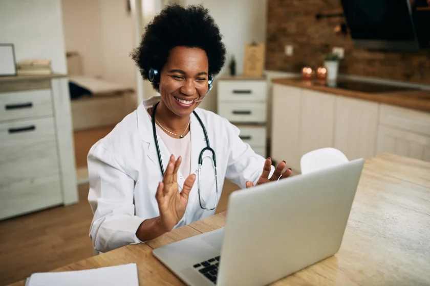 smiling female healthcare worker conducting telemedicine appointment on computer