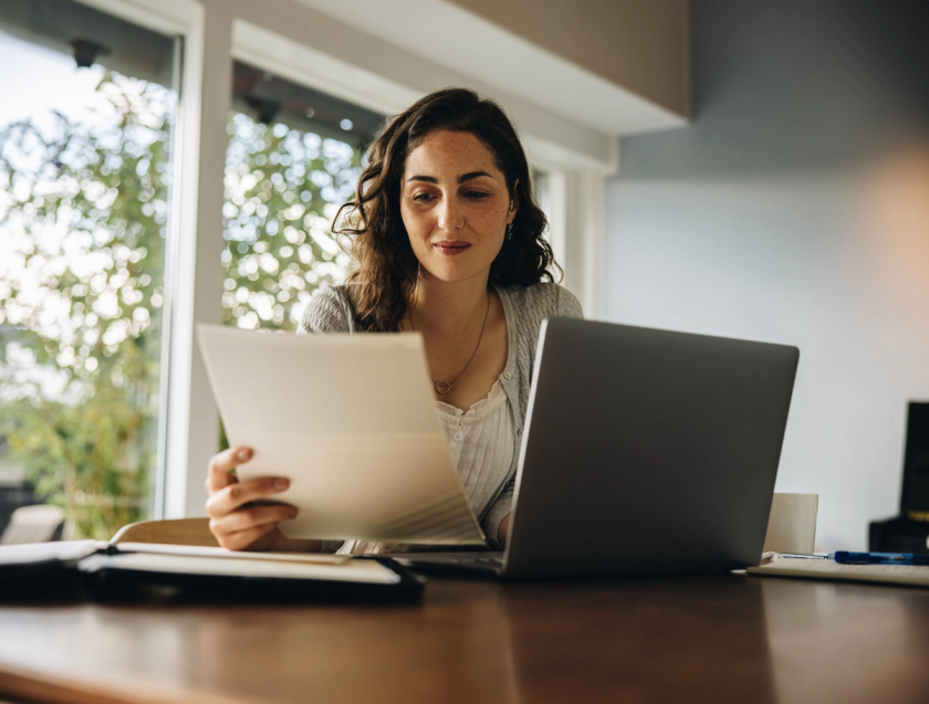 Woman in office reading paper in front of laptop