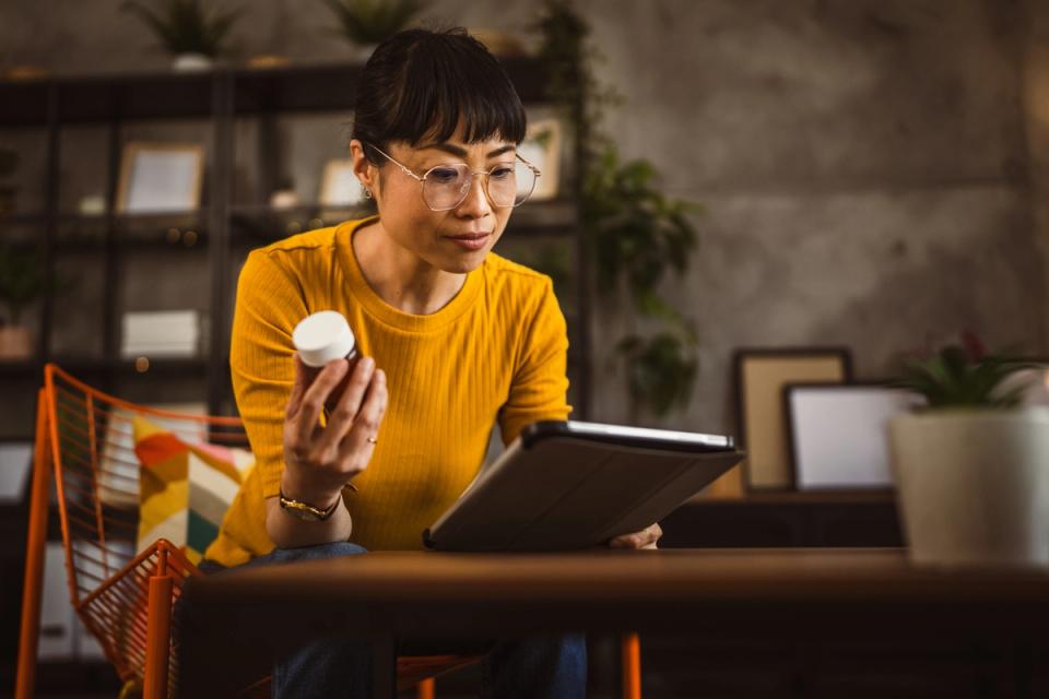Women looking for information online on a tablet about the bottle of dietary supplements she's holding.