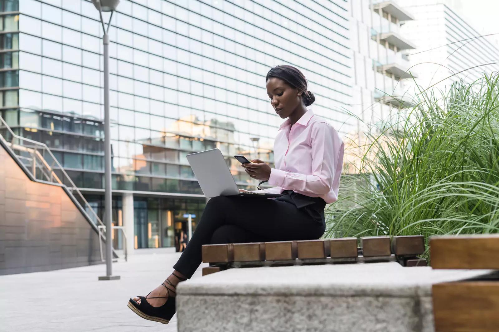 Woman sitting on bench outside working on laptop