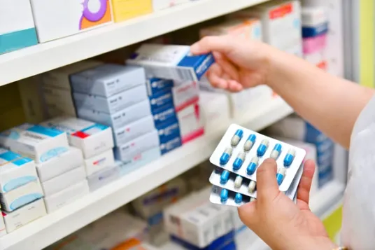 pharmacist holding medications and placing them on pharmacy shelf