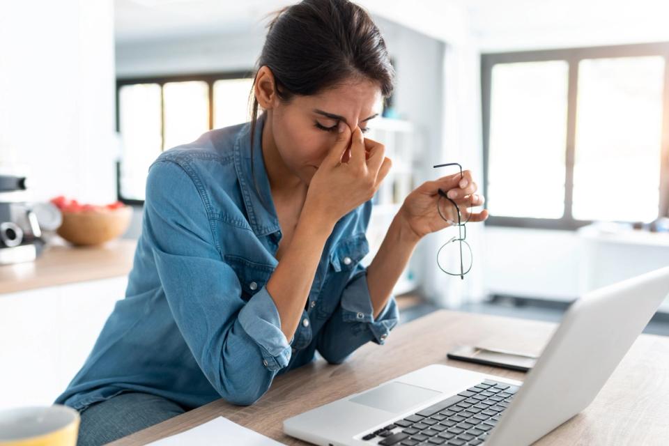 Women pinching her nose sitting at desk.