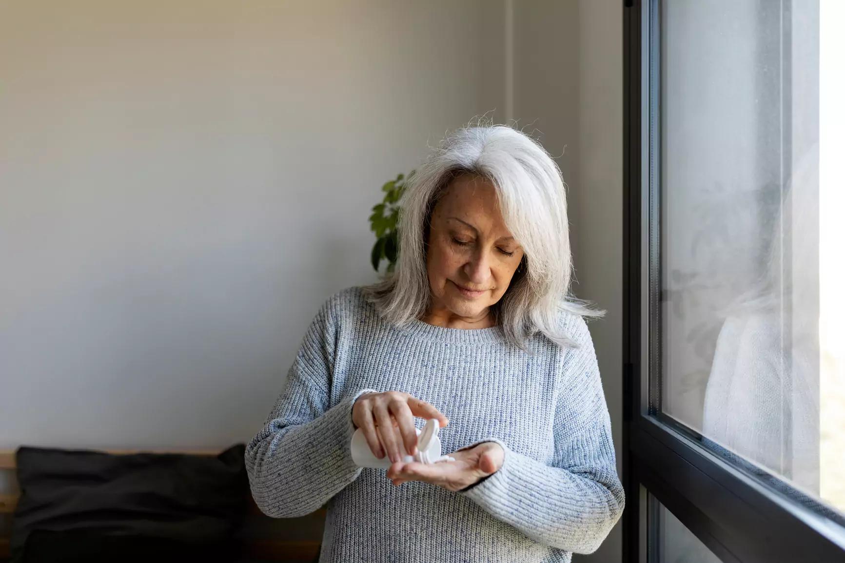 Woman dispensing pills into hand from pill bottle
