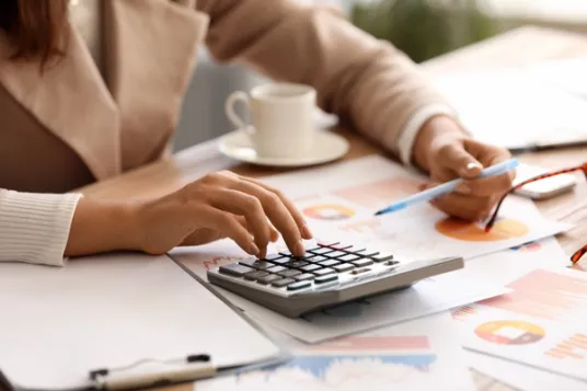 Young Businesswoman Working with Documents and Calculator at Workplace in Office, Closeup