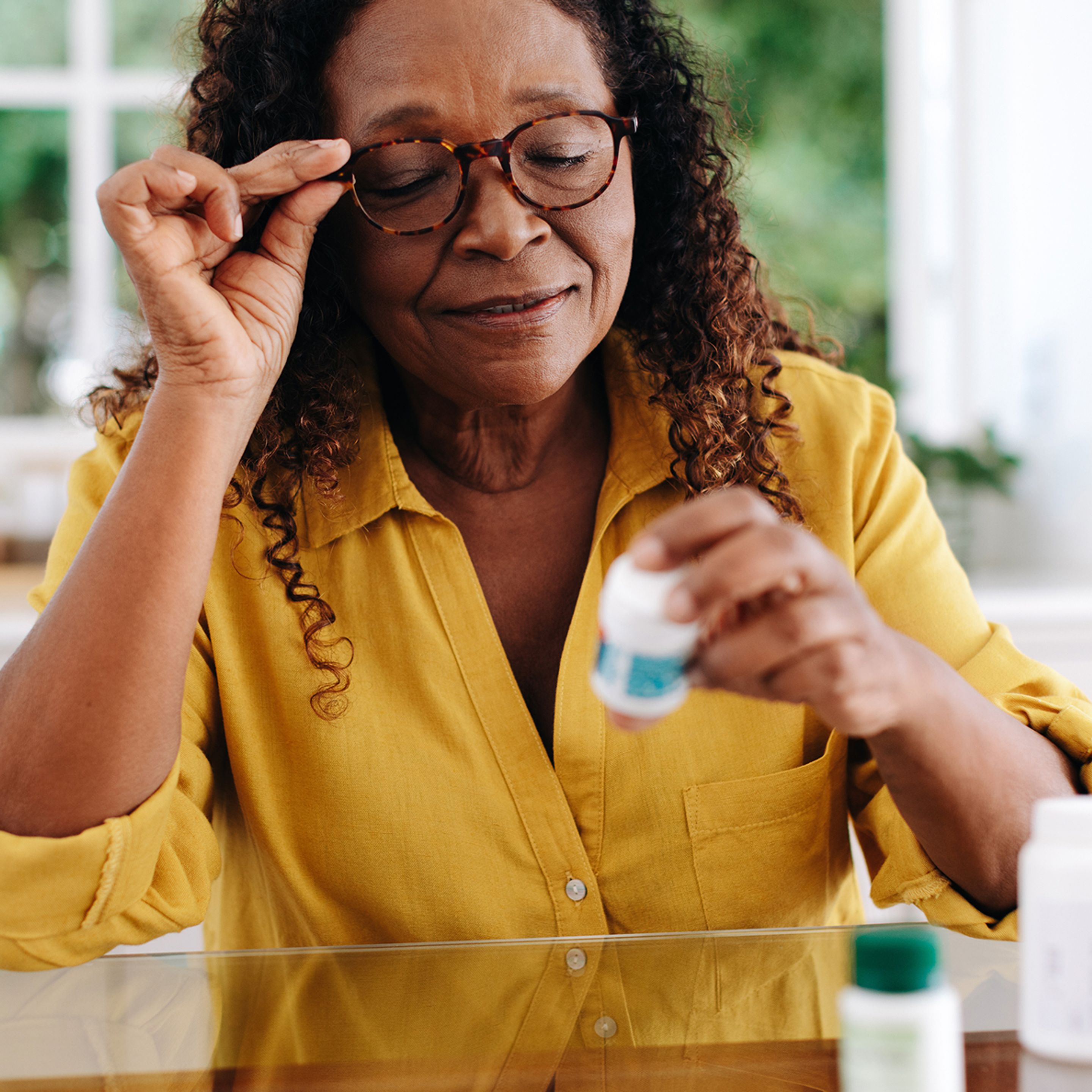 Woman in yellow shirt with glasses looking at medicine bottle