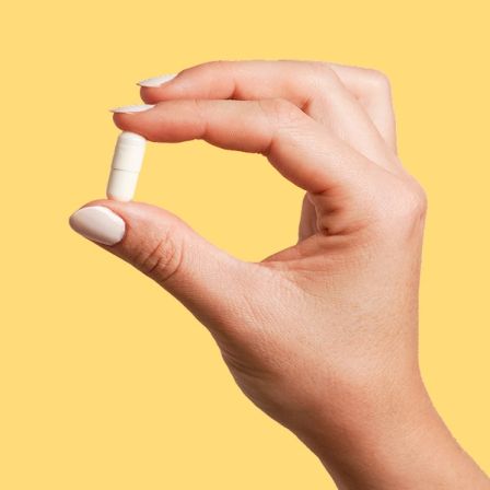 Yellow background with hand holding a pill