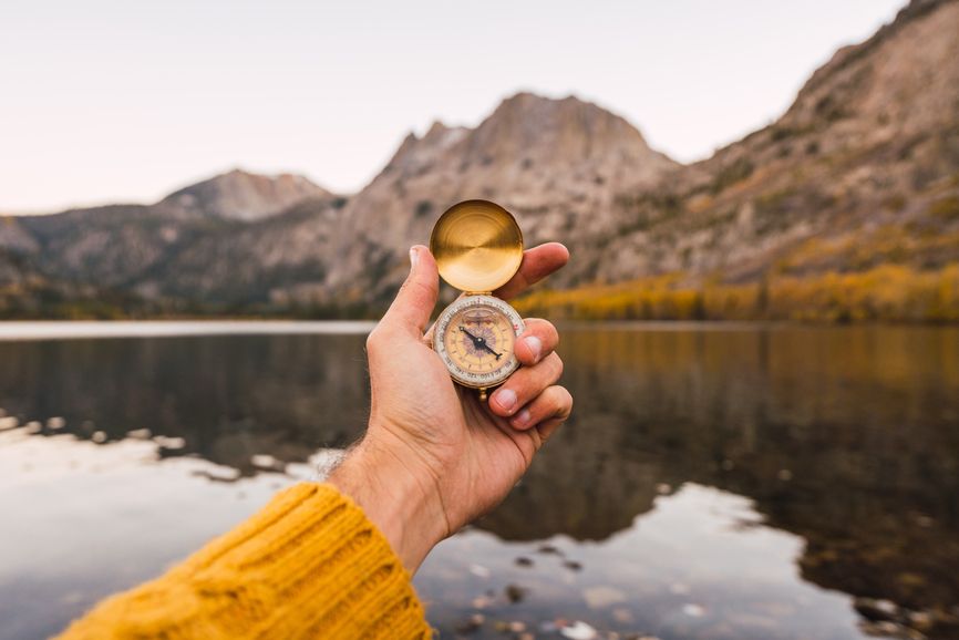 Hand holding compass with lake and mountains in background