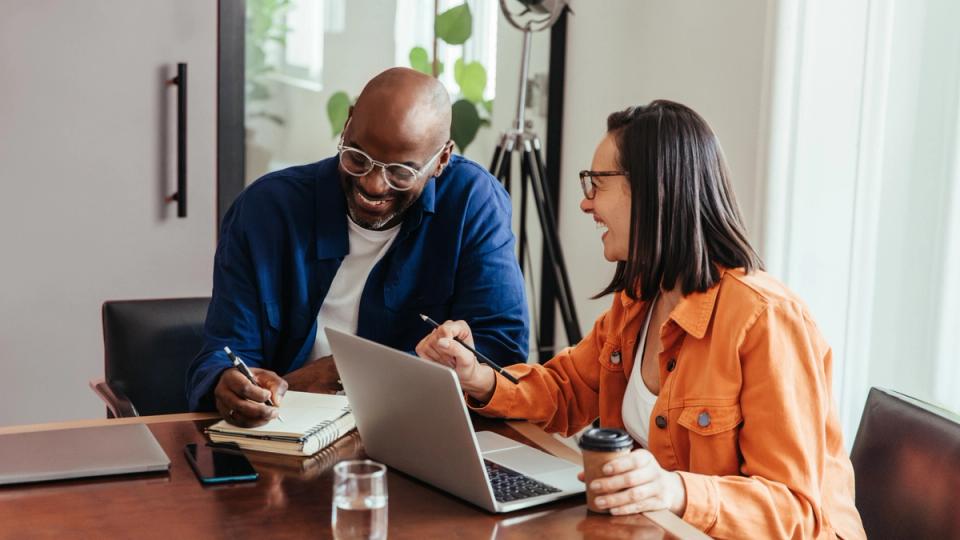 Two coworkers smiling and working on laptop