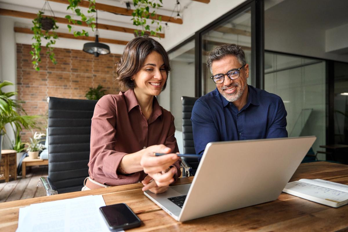 Two coworkers smiling and working on laptop