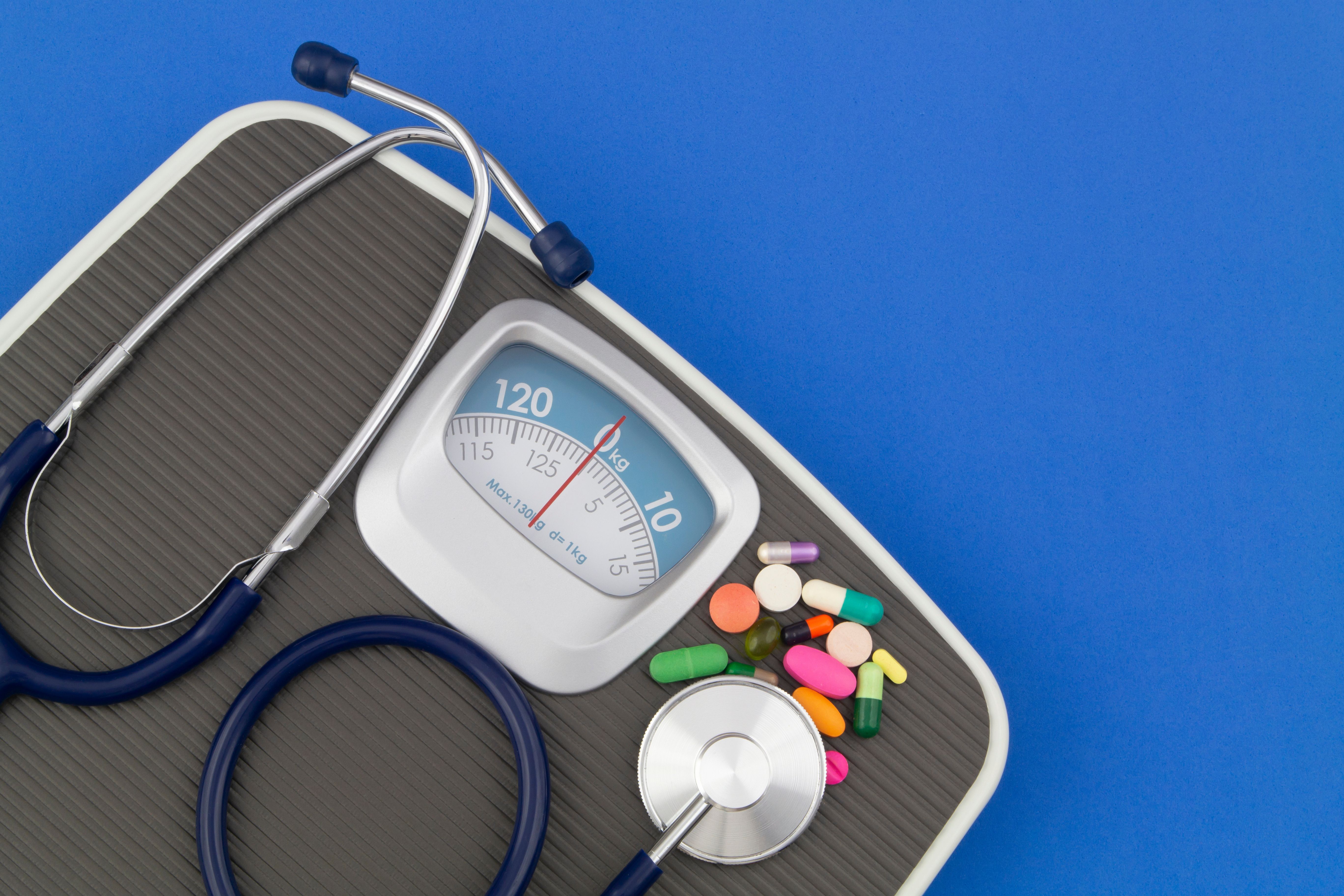 Scale with stethoscope and pills on top with dark blue background