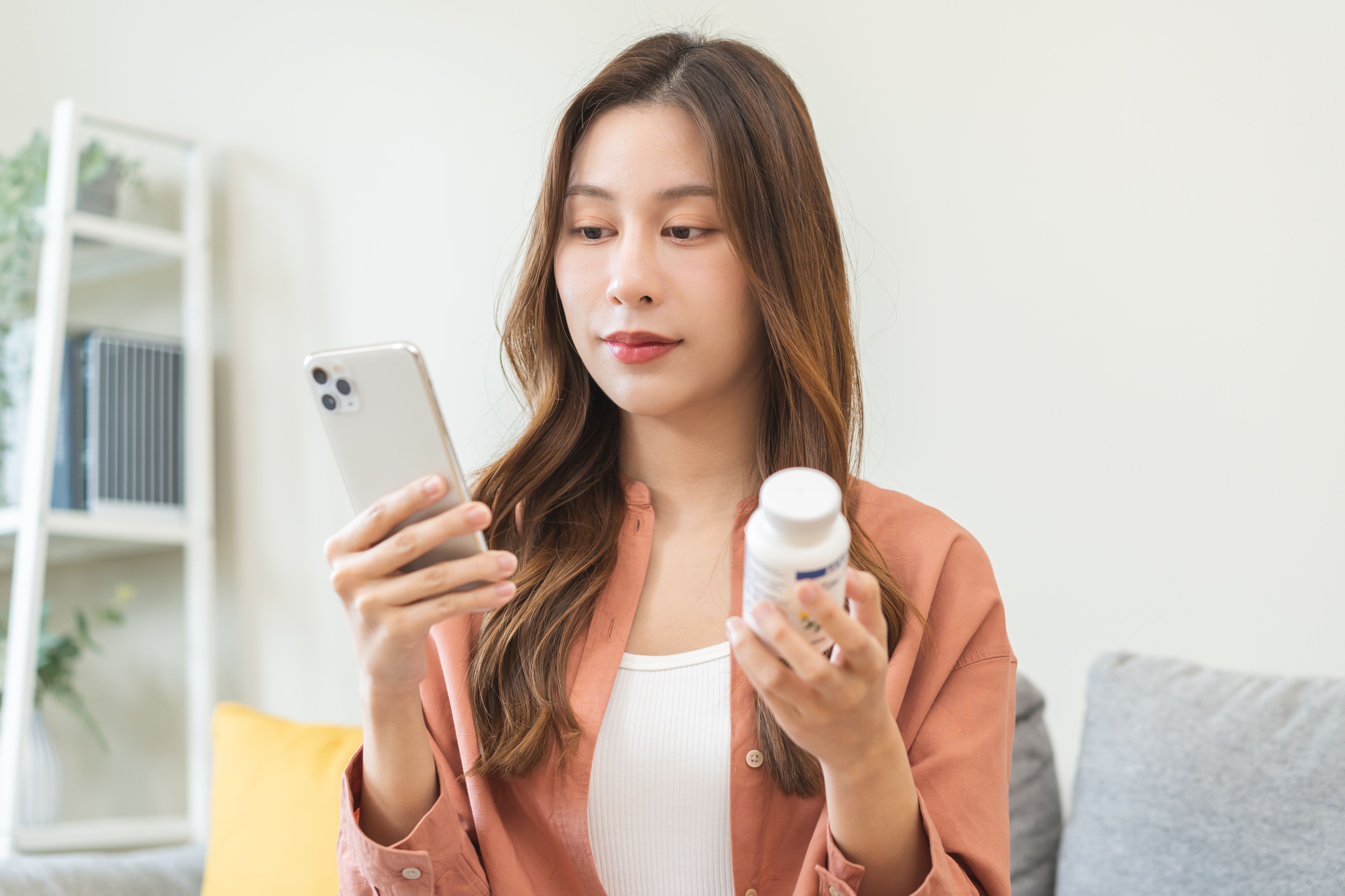 Woman looking at phone and holding pill bottle