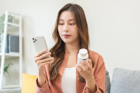 Woman looking at phone and holding pill bottle