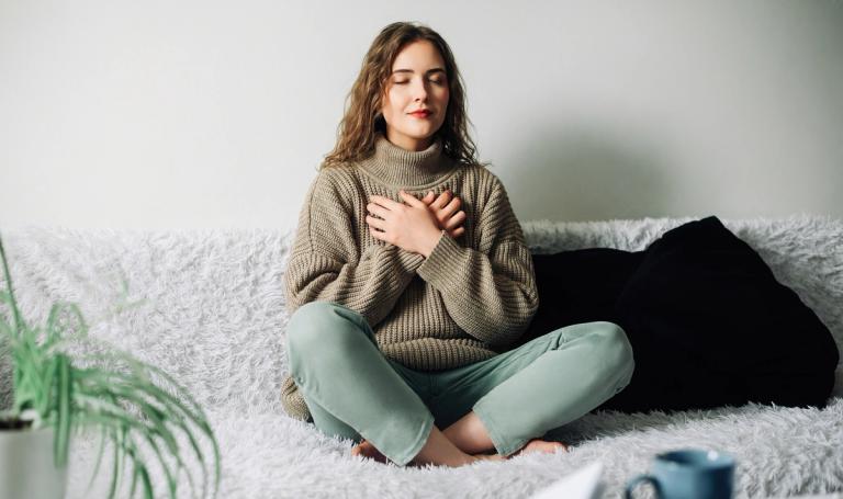 Woman sitting criss-cross on a couch doing deep breathing exercises.