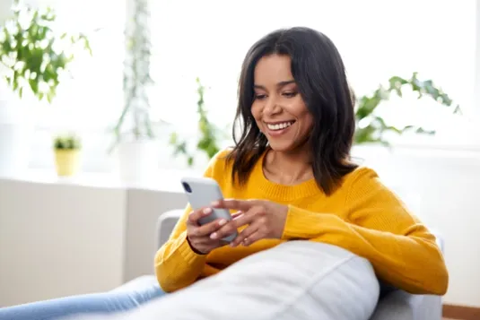 Woman in yellow shirt looking at phone and smili