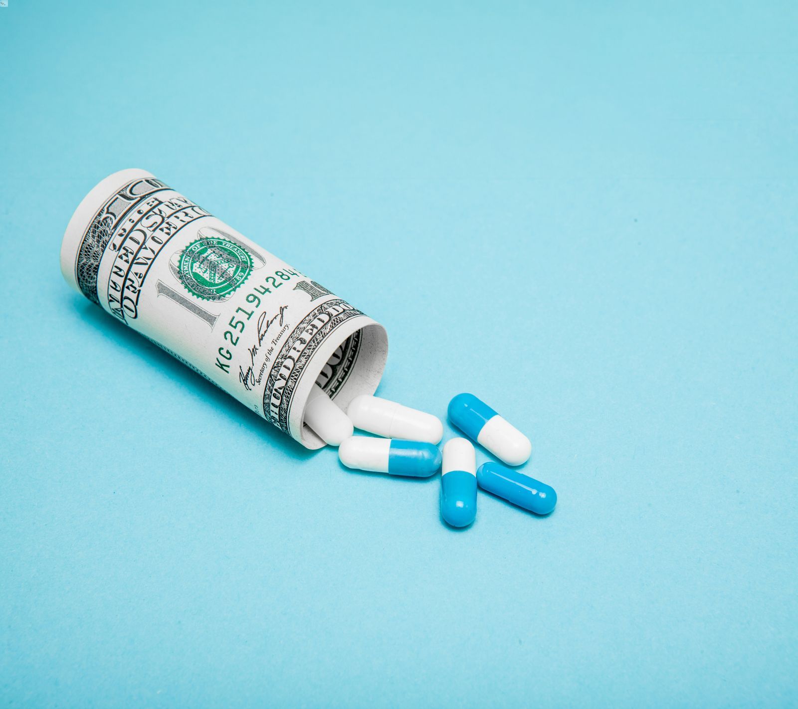 Rolled up money in the shape of a pill bottle with pills spilling out