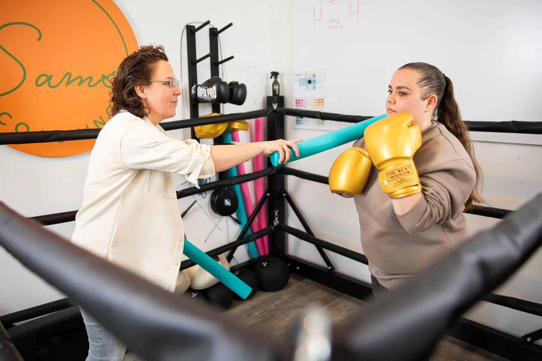 Samantha oefent met een jongere met gouden handschoenen en foamstokken