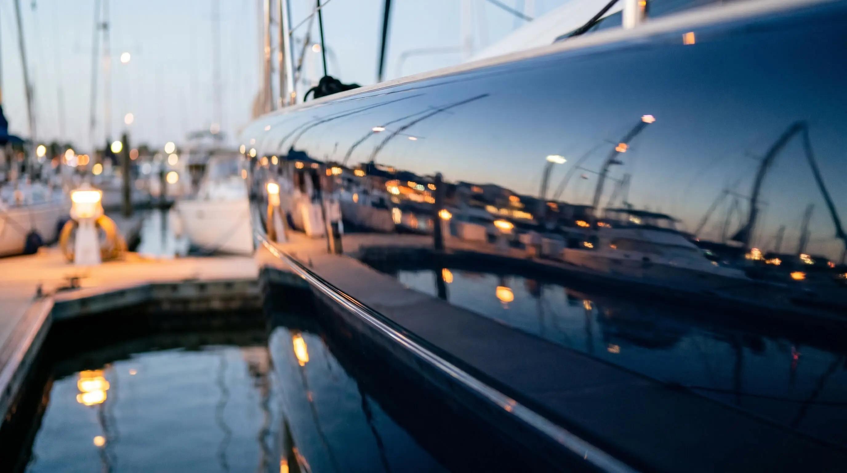 Close-up van een gepolijste donkere jachtromp met spiegeling van havenverlichting en masten in het gelcoat oppervlak