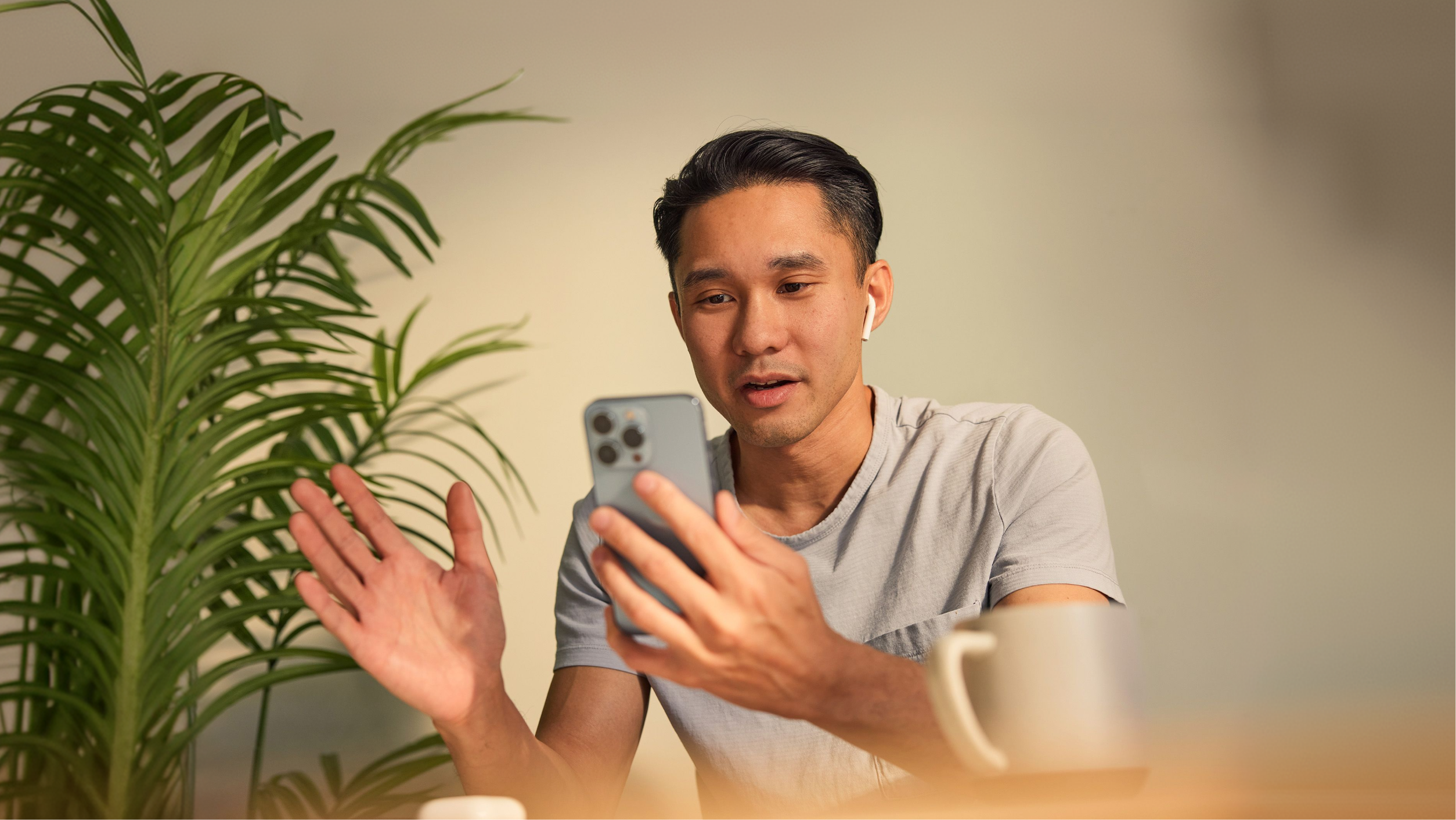 Man practicing English speaking on a video call, gesturing as he talks into his phone with one earbud in