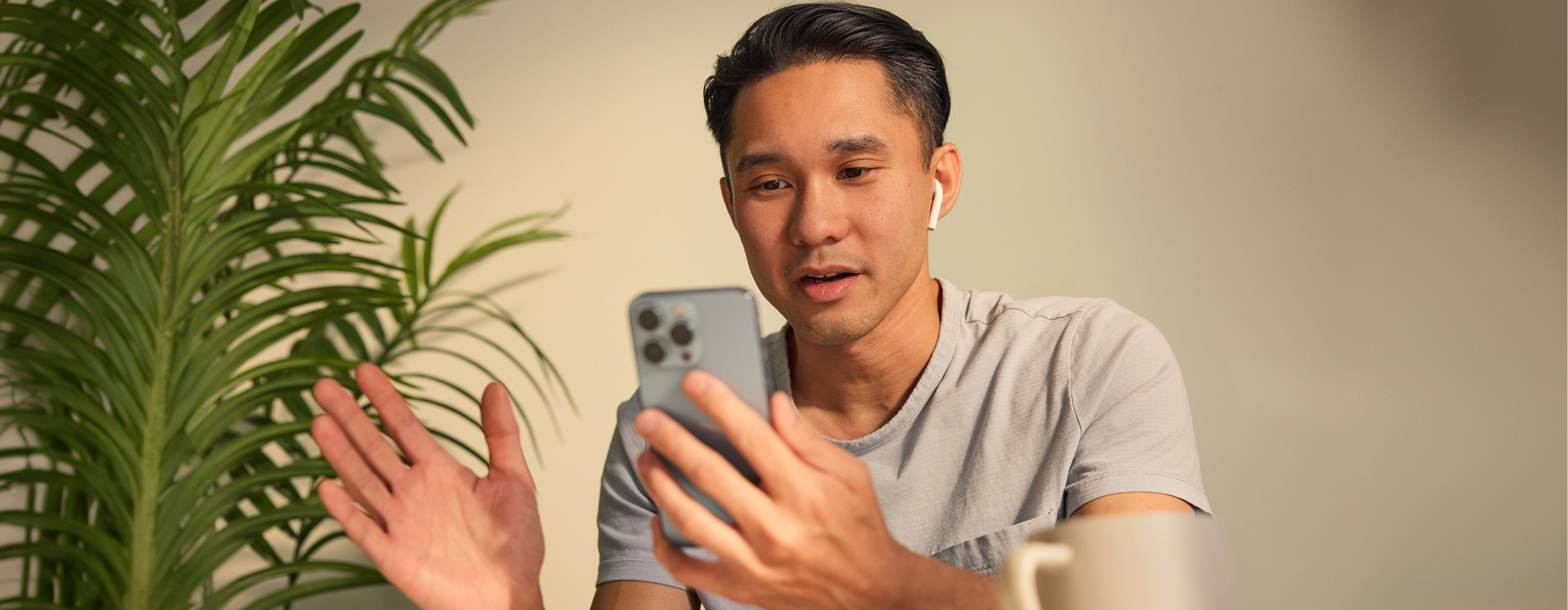 Man practicing English speaking on a video call, gesturing as he talks into his phone with one earbud in