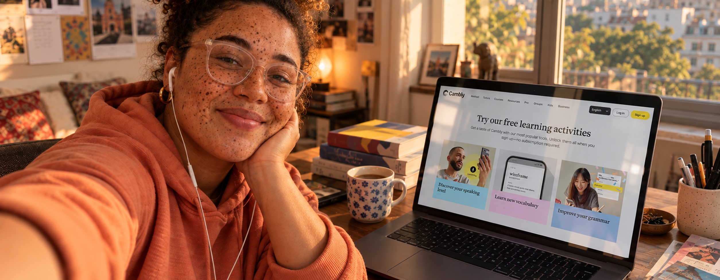 Mulher de fone de ouvido sorrindo em frente ao notebook aberto na página de atividades gratuitas do Cambly, com caderno, caneta e livros sobre a mesa.