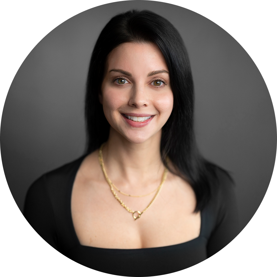 Woman with dark hair and a black square-neck top smiling at the camera. She wears a gold necklace. Gray background.