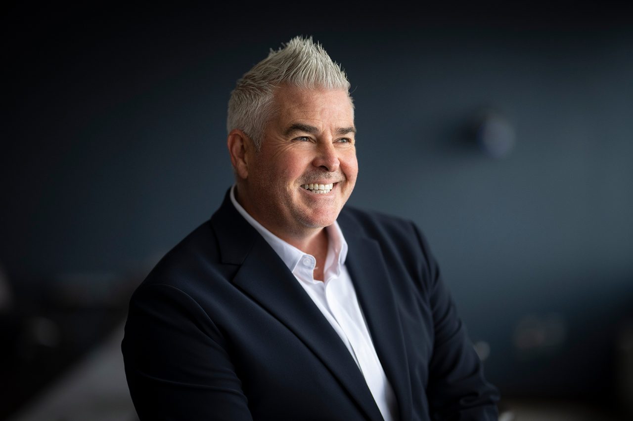 Smiling man in a suit with gray hair looking to the side.