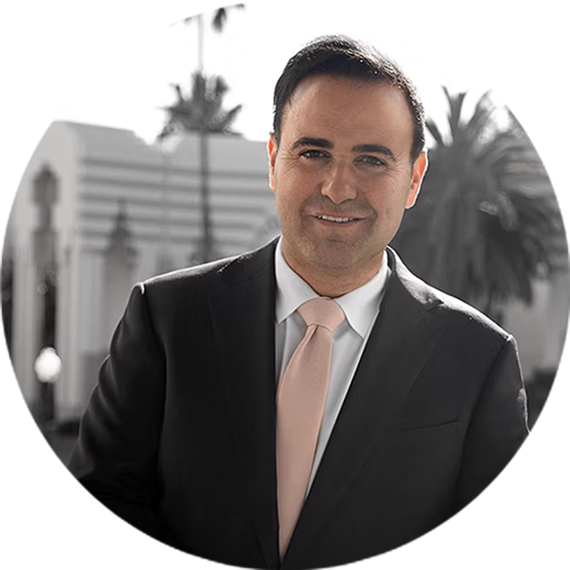 Man in suit with pink tie smiling. Palm trees and building in grayscale background.