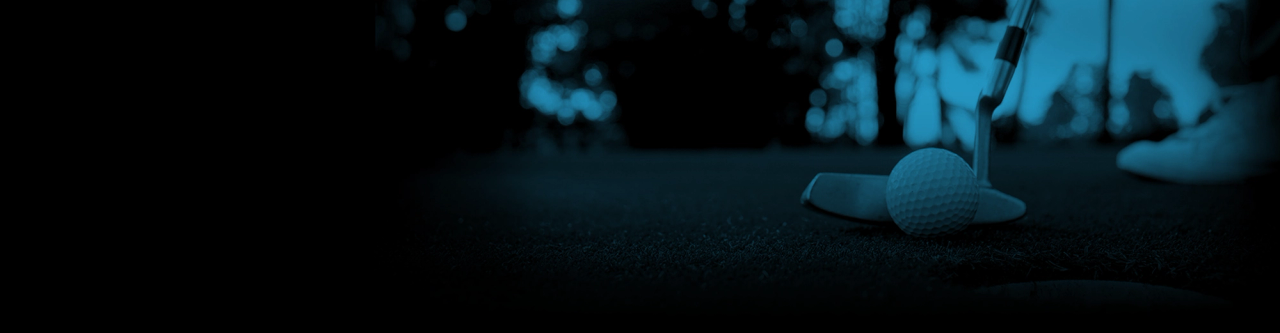 Close up of a golf ball next to a putter on the green, near the hole.
