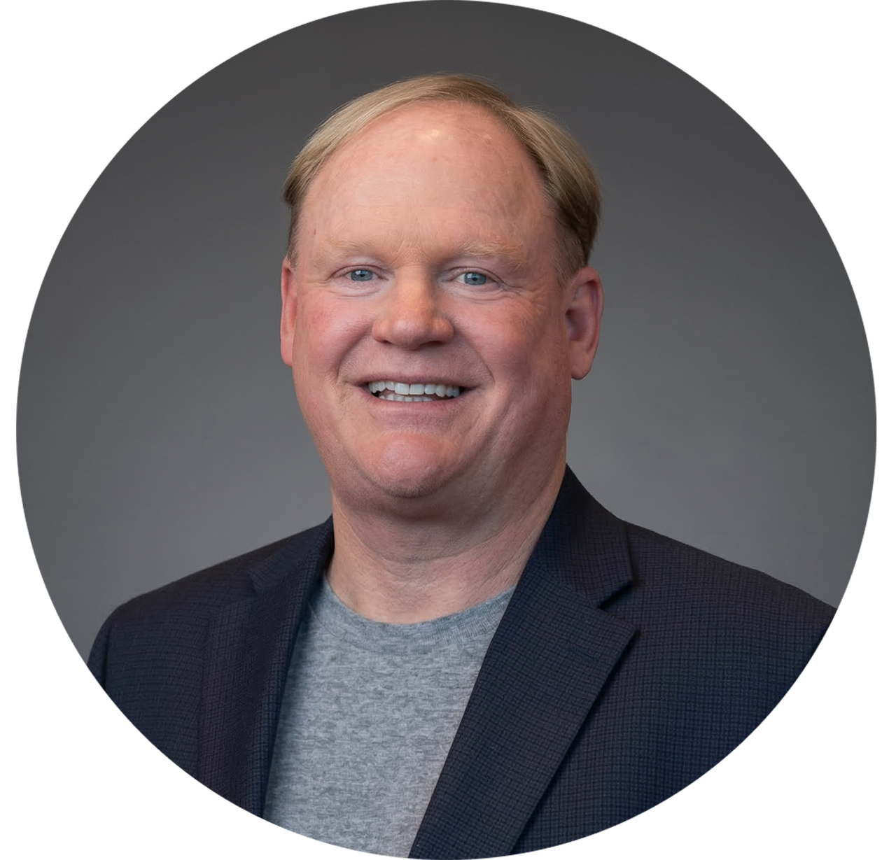Smiling man in blazer over gray t-shirt, presented in a circular frame.