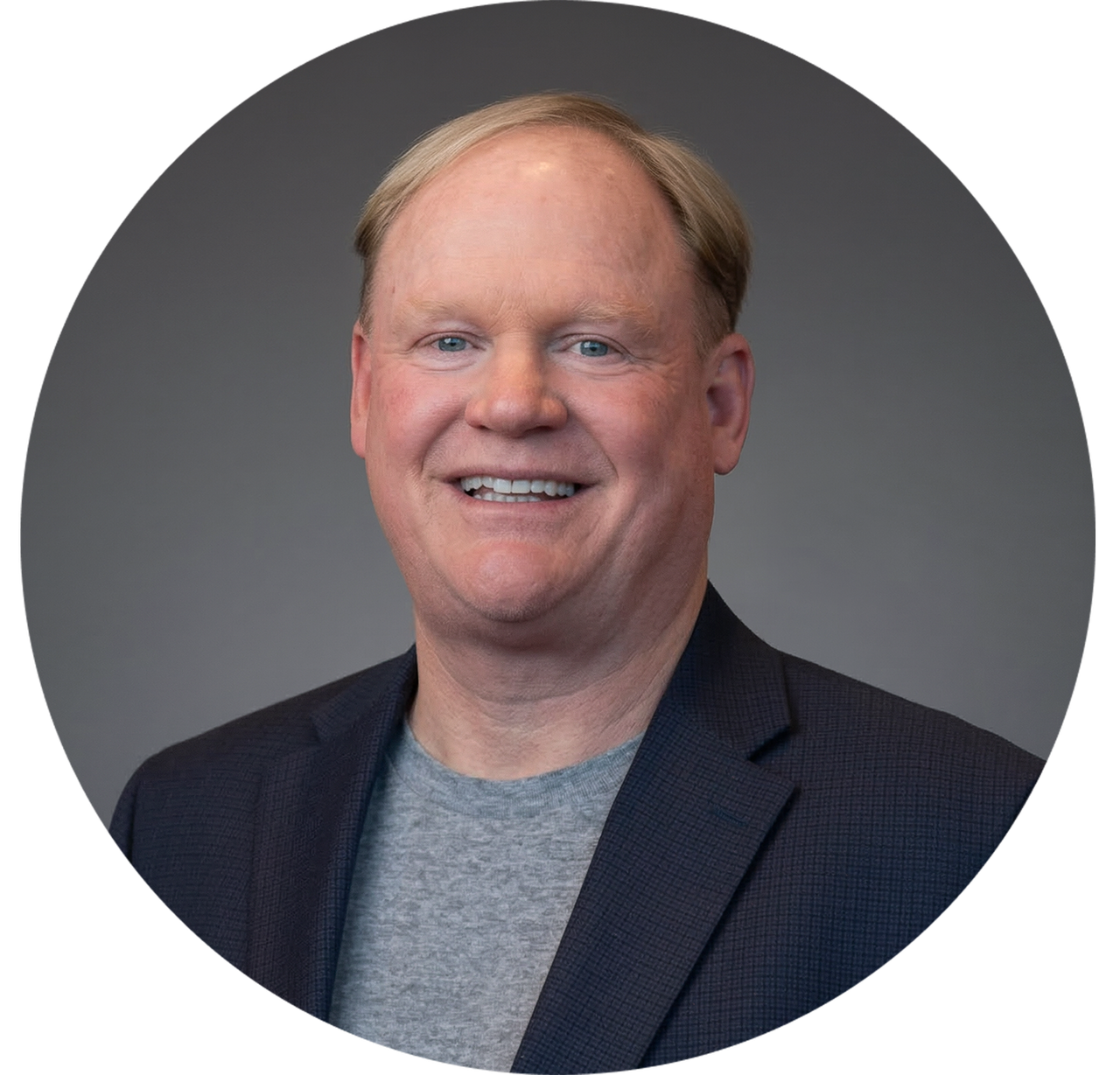Smiling man in blazer over gray t-shirt, presented in a circular frame.
