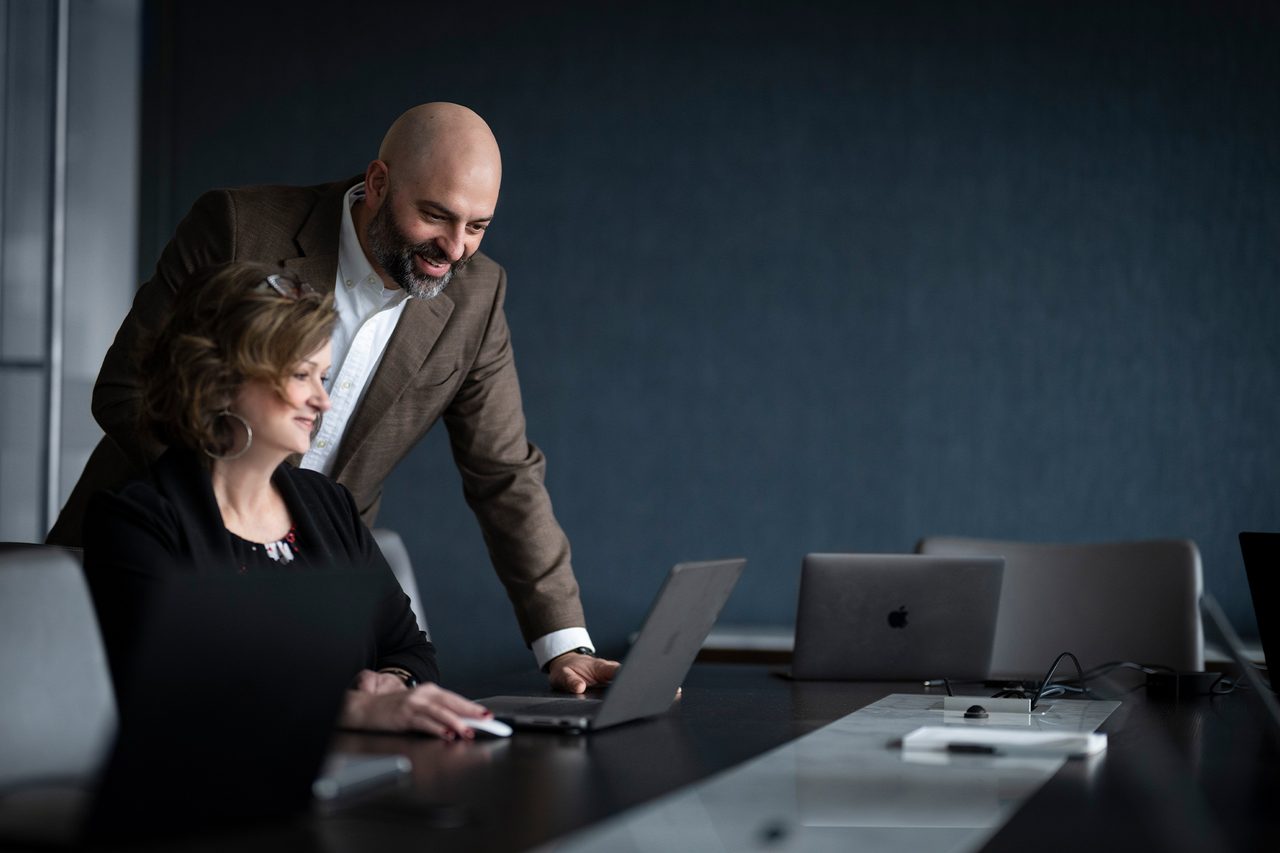 Two businesspeople looking at a laptop in a conference room. They appear to be collaborating.