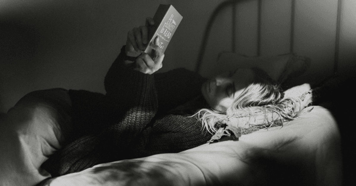 Person reading a book in bed, low light