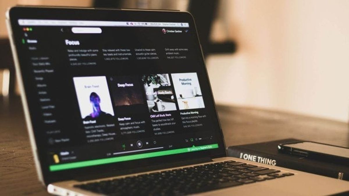 Laptop displaying Spotify playlists on wooden desk.